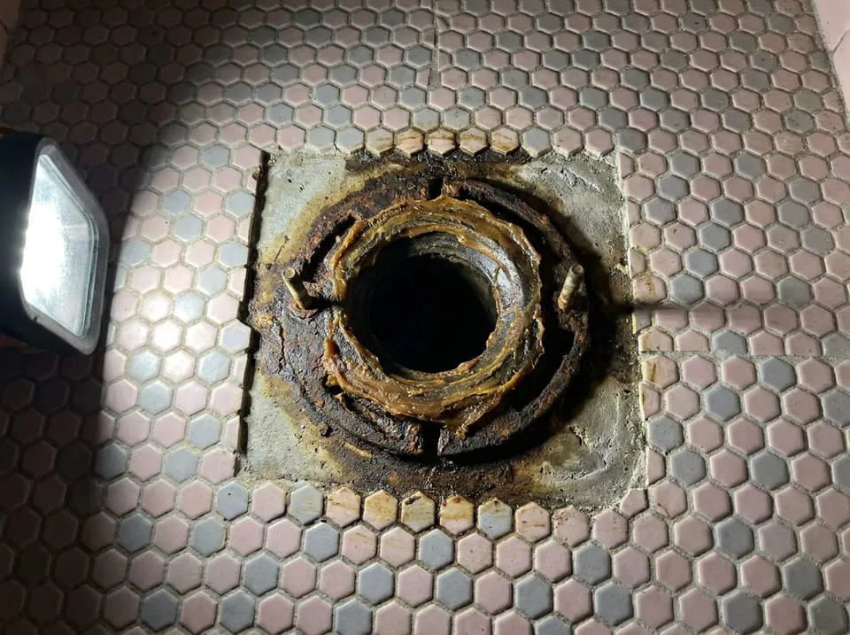 Pulled toilet exposing a flattened wax ring on a rusty cast iron closet flange, a source of sewer smell in a bathroom