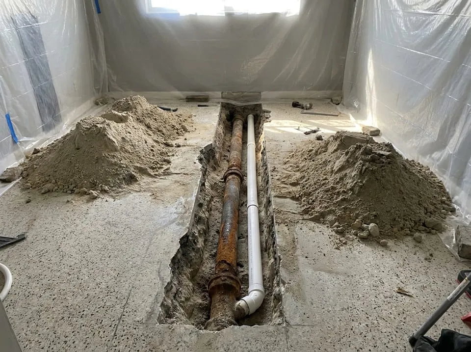 Saw-cut trench through a terrazzo floor exposing old cast iron drain pipe under a Florida slab